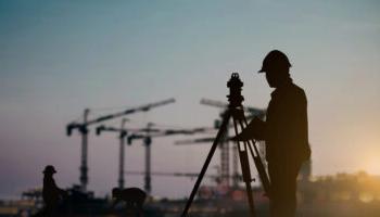 An Image Of A Surveyor Taking Measurements In The Foreground Of A Large Construction Site.